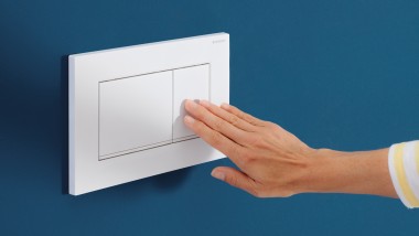 Hand löst auf der weißen Sigma20 Betätigungsplatte eine Spülung aus (© Geberit)