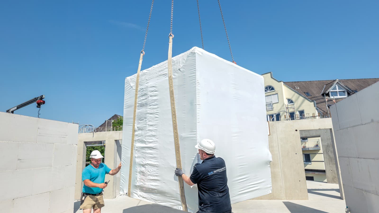 Monteure nehmen das vorgefertigte Badmodul vom Kran an Monteure nehmen das vorgefertigte Badmodul vom Kran an